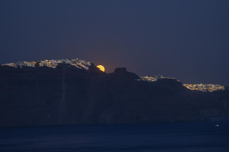 The moon rises behind the village of Imerovigli, left, and the rocky promontory of Skaros, right, on the Greek island of Santorini on Tuesday, June 14, 2022. The Catholic Monastery of St. Catherine was founded at Skaros in 1596, but after an earthquake it was moved to the town of Thira, far right. (AP Photo/Petros Giannakouris)