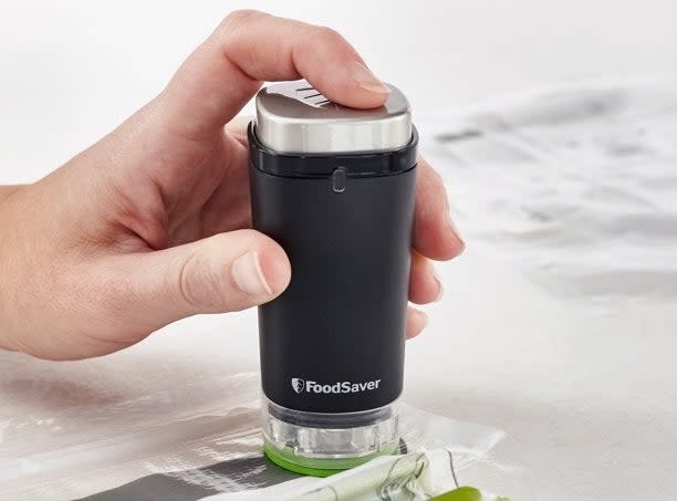 Someone holding the small handheld sealer over a vacuum seal bag and pull excess air out to store and preserve fresh celery stalks