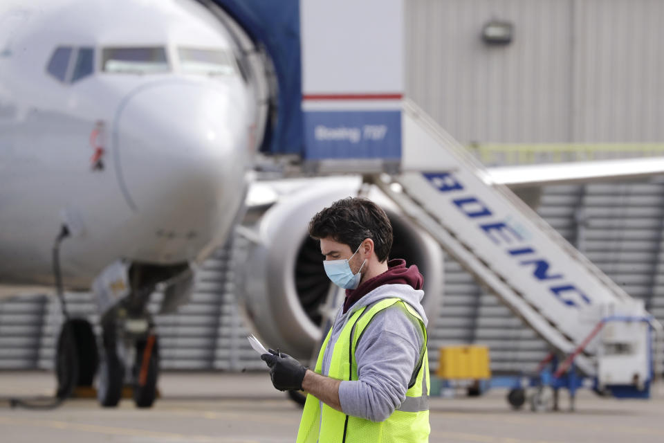 A worker walks past a Boeing 737 MAX jet at a Boeing airplane manufacturing plant Wednesday, April 29, 2020, in Renton, Wash. Boeing says it will cut about 10% of its workforce and slow production of planes as it deals with the ongoing grounding of its best-selling plane and the coronavirus pandemic. With air travel falling sharply because of the virus, airlines have delayed orders and deliveries of new planes, reducing Boeing's revenue. (AP Photo/Elaine Thompson)