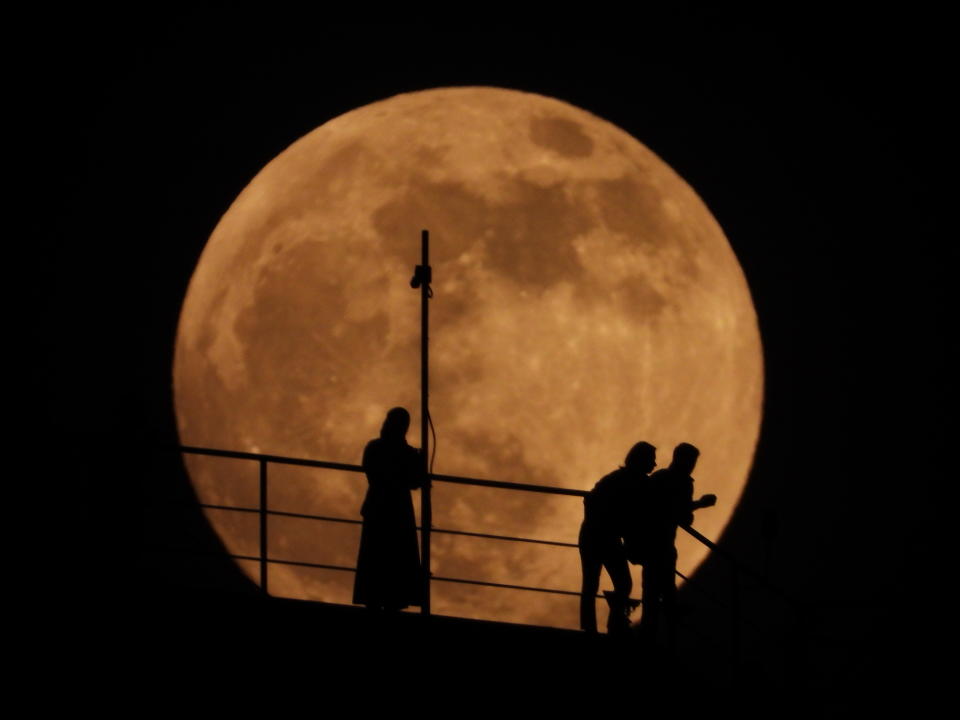 People are silhouetted as an almost full moon rises above the sky in Grozny, Russia, Sunday, May 15, 2022. (AP Photo/Musa Sadulayev)