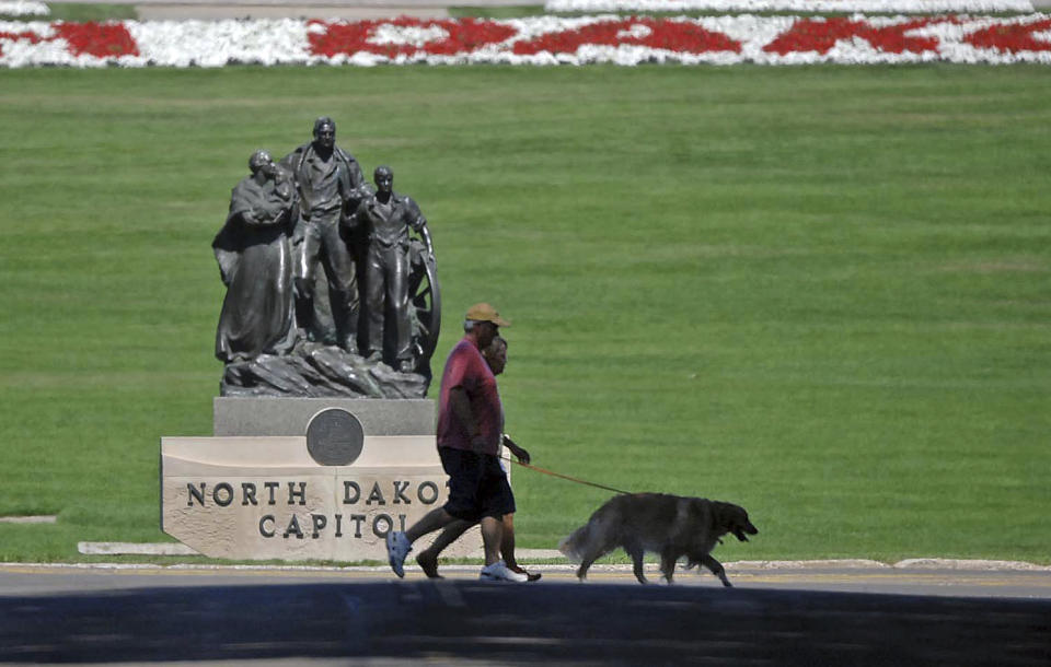 FILE - In this Aug. 19, 2013 file photo, people walk a dog across Sixth Street in front of the state capitol in Bismarck, N.D. Lawmakers are trying to stop 144 cities across the U.S. from losing their designations as “metropolitan areas” because the federal government is upgrading the standard from a minimum of 50,000 residents in its core to a minimum of 100,000 people. Bismark is among those at risk of losing the designation. (Tom Stromme/The Bismarck Tribune via AP, File)