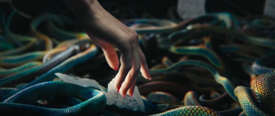 A hand reaches down into a pit of mutated rainbow snakes in The Hunger Games prequel movie trailer to retrieve a piece of paper.