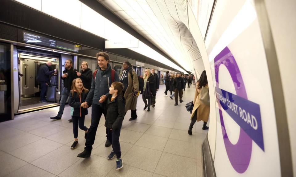 People using the Elizabeth line at Tottenham Court Road station: in the foreground, a man walking on the platform with his two children.