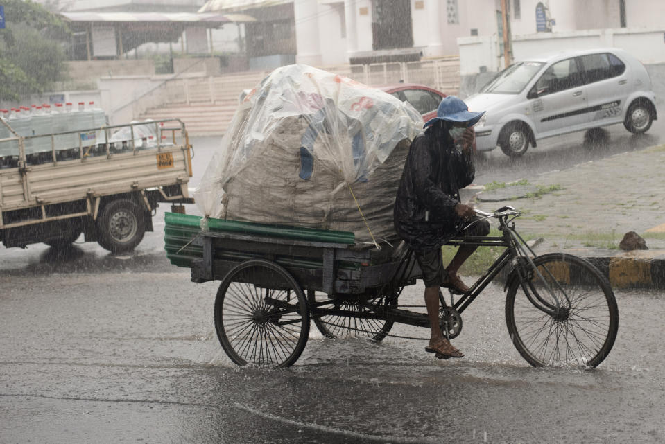 A man wearing a mask as a precaution against the coronavirus pedals his rickshaw during heavy rainfall in Kochi, Kerala state, India, Friday, Aug.7, 2020. A mudslide triggered by heavy monsoon rain and flooding killed at least five people in the state on Friday, police said. (AP Photo/R S Iyer)