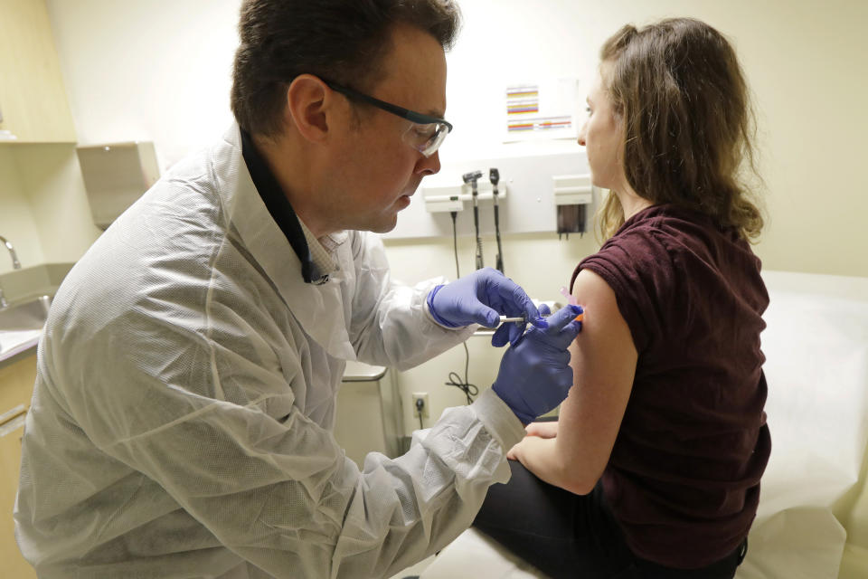 Pharmacist Michael Witte, left, gives Rebecca Sirull, right, a shot in the first-stage safety study clinical trial of a potential vaccine for COVID-19, the disease caused by the new coronavirus, Monday, March 16, 2020, at the Kaiser Permanente Washington Health Research Institute in Seattle. Sirull is the third patient to receive the shot in the study. (AP Photo/Ted S. Warren)