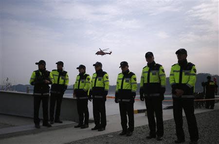 Police officers are seen as a rescue and salvage team helicopter (top) flies over a port where family members of missing passengers from the capsized passenger ship Sewol gathered to wait for news from rescue and salvage teams, in Jindo April 22, 2014. REUTERS/Kim Hong-Ji