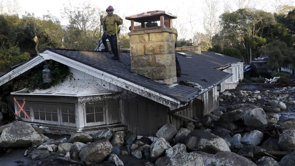 Ein Feuerwehrmann steht auf dem Dach eines Hauses, das nach einem Erdrutsch in Montecito, Kalifornien, im Jahr 2018 in Schlamm und Steinen versunken ist. – Marcio Jose Sanchez/AP