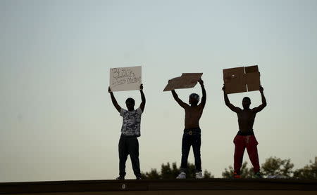 Protesters hold up signs on top of a closed business in Ferguson, Missouri, August 10, 2015. Protesters regrouped in Ferguson, Missouri, on Monday evening after a state of emergency was declared, aimed at preventing a repeat of violence the night before on the anniversary of the police shooting of unarmed black man Michael Brown. REUTERS/Rick Wilking