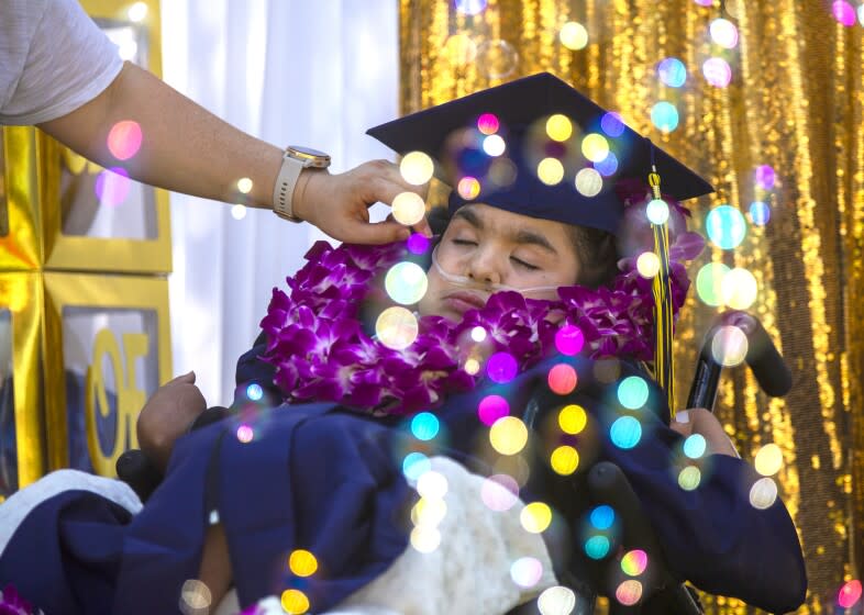 WHITTIER, CA - MAY 16: Wearing her deep Rembrandt blue cap and gown, Hannah Lopez, 18, attends attend her early graduation ceremony in her front yard May 16, 2021 in Whittier, CA. Her little sister Paloma is playing with a small portable bubble machine near Hannah. The bubbles float past her reflecting light. (Francine Orr / Los Angeles Times)