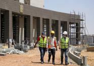 Construction workers walk beside a complex of government buildings under construction in the New Administrative Capital (NAC), east of Cairo