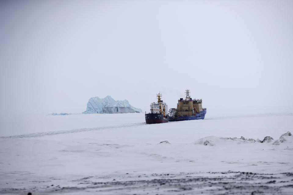 An Icebreaker making the path for a cargo ship with an iceberg in the background near a port on the Alexandra Land island near Nagurskoye, Russia, Monday, May 17, 2021. (AP Photo/Alexander Zemlianichenko)