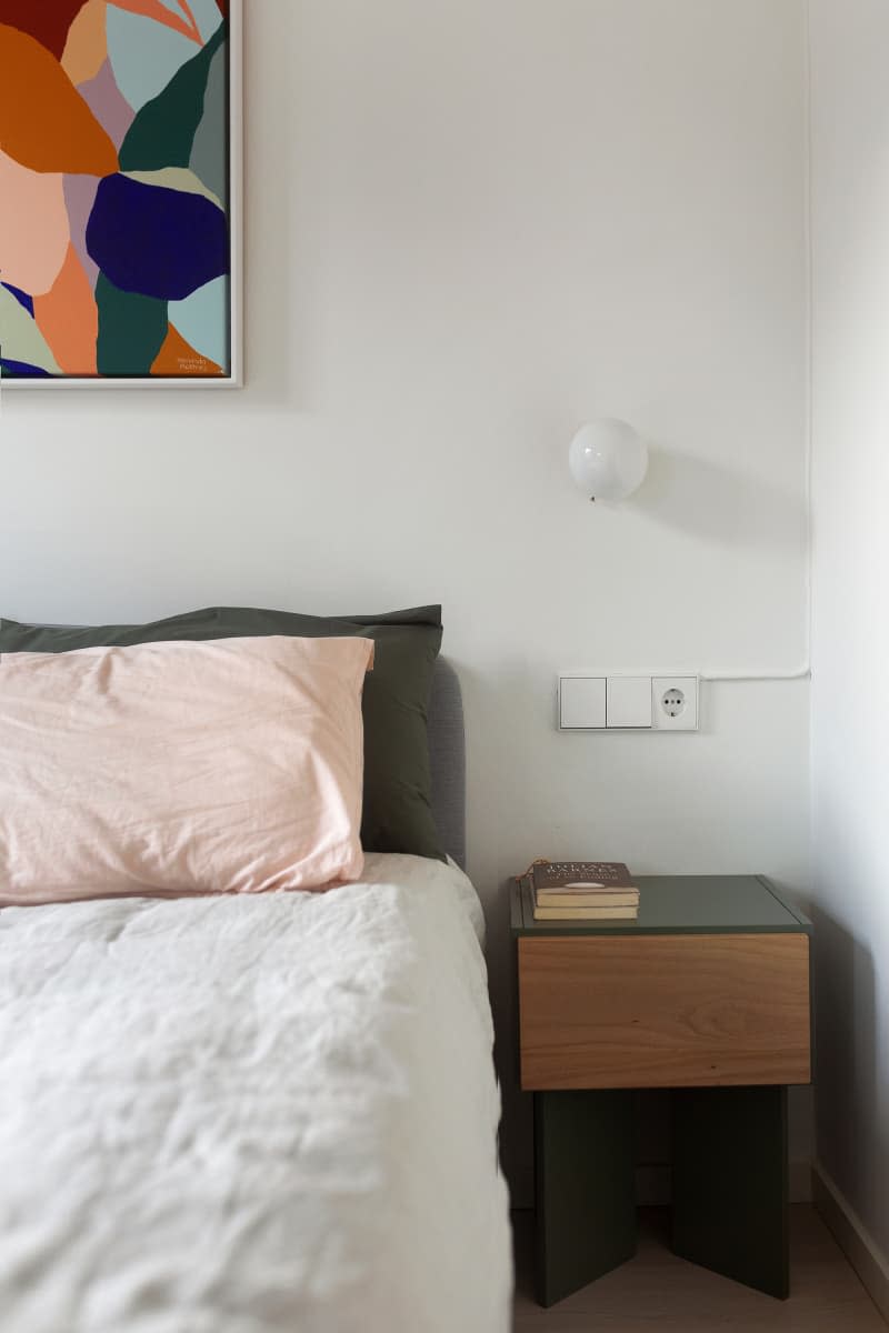 Bed with pink and dark green pillow next to a wooden bedside table.