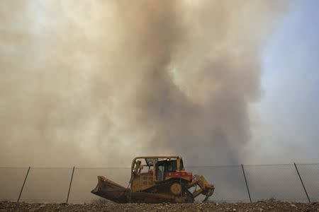 Smoke rises behind a firefighting bulldozer as a wildfire driven by fierce Santa Ana winds blows in Rancho Cucamonga, California, April 30, 2014. REUTERS/David McNew