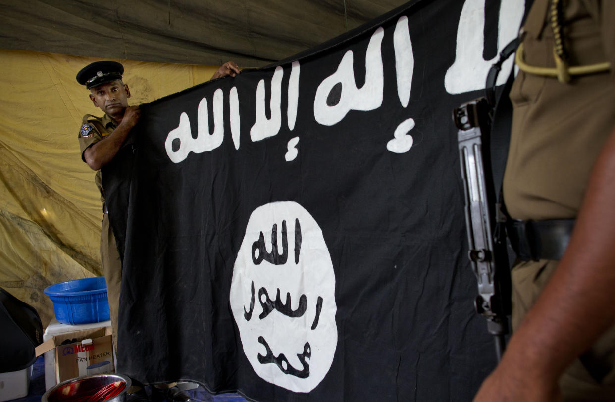 Police officers display a flag in Arabic that reads: "There is no god, but Allah" and "Of Allah is the Prophet, Muhammad" in Ampara, Sri Lanka, Sunday, April 28, 2019. Police in Ampara showed The Associated Press on Sunday the explosives, chemicals and Islamic State flag they recovered from the site of one security force raid in the region as Sri Lanka's Catholics celebrated at televised Mass in the safety of their homes. (AP Photo/Gemunu Amarasinghe)