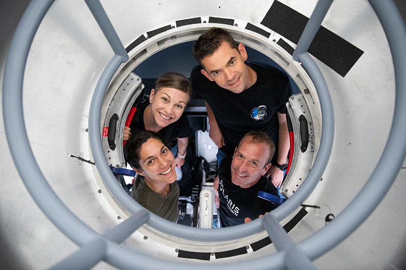 The crew of Polaris Dawn look up through the hatch of a Crew Dragon simulator, framed by a scaffolding known as the 