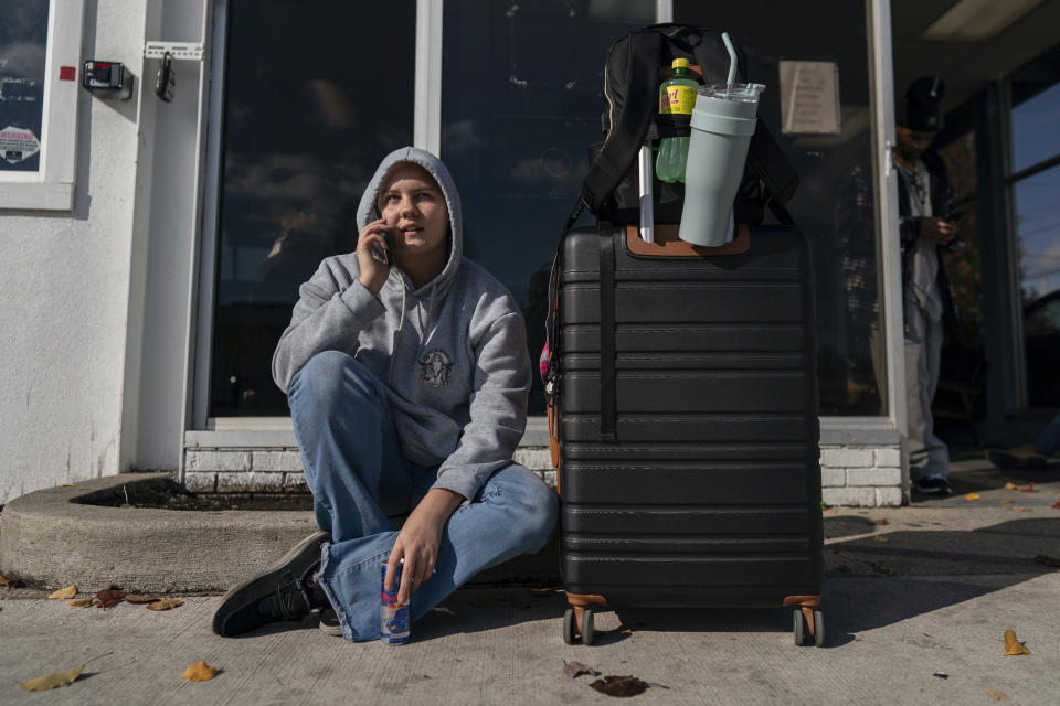 Joceline Grubb talks on a cell phone sitting on the curb outside the entrance to the Greyhound's Dayton Trotwood Bus Station in Dayton, Ohio, Wednesday, Nov. 22, 2023. Grubb is waiting for a bus to London, Ky., for Thanksgiving. Despite inflation and memories of past holiday travel meltdowns, millions of people are expected to hit airports and highways in record numbers over the Thanksgiving Day break. (AP Photo/Carolyn Kaster)