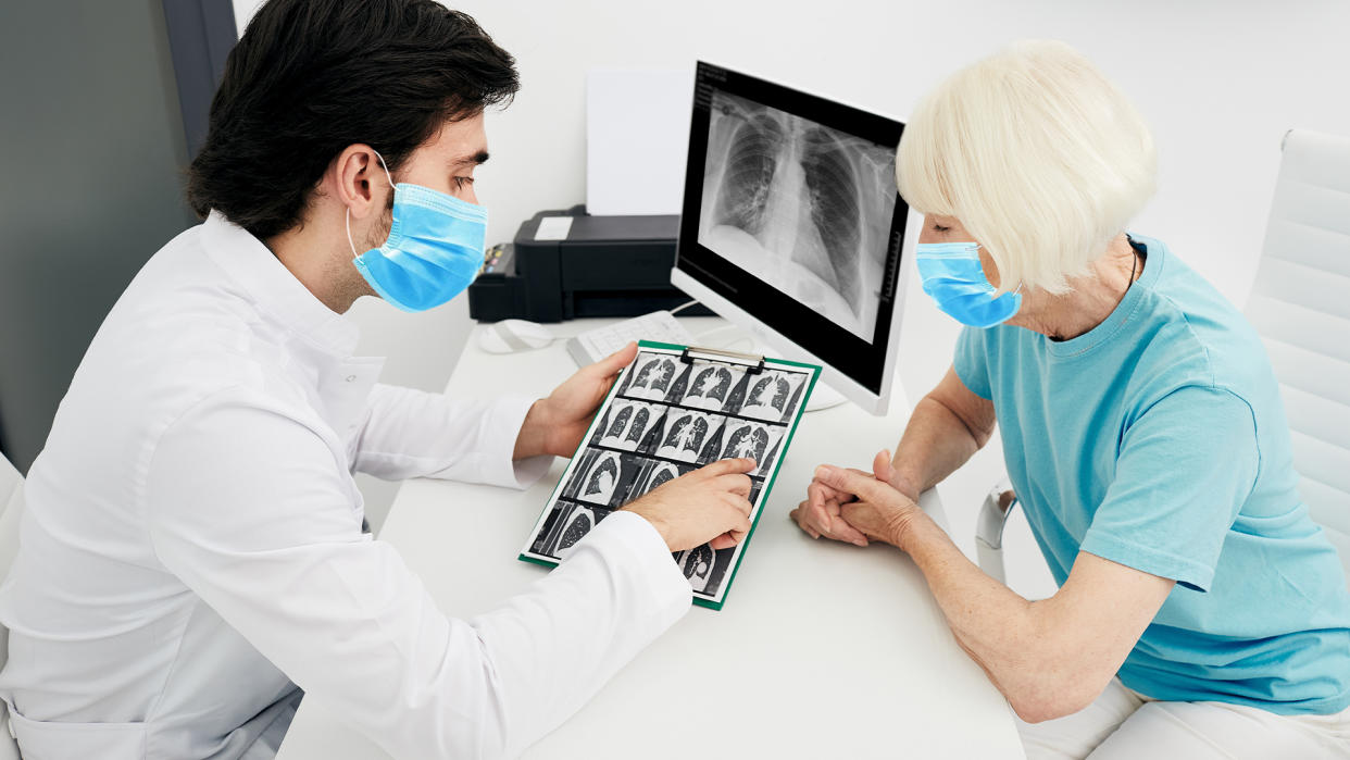  Pulmonologist wearing a surgical mask showing a senior patient a CT scan of her lungs. 