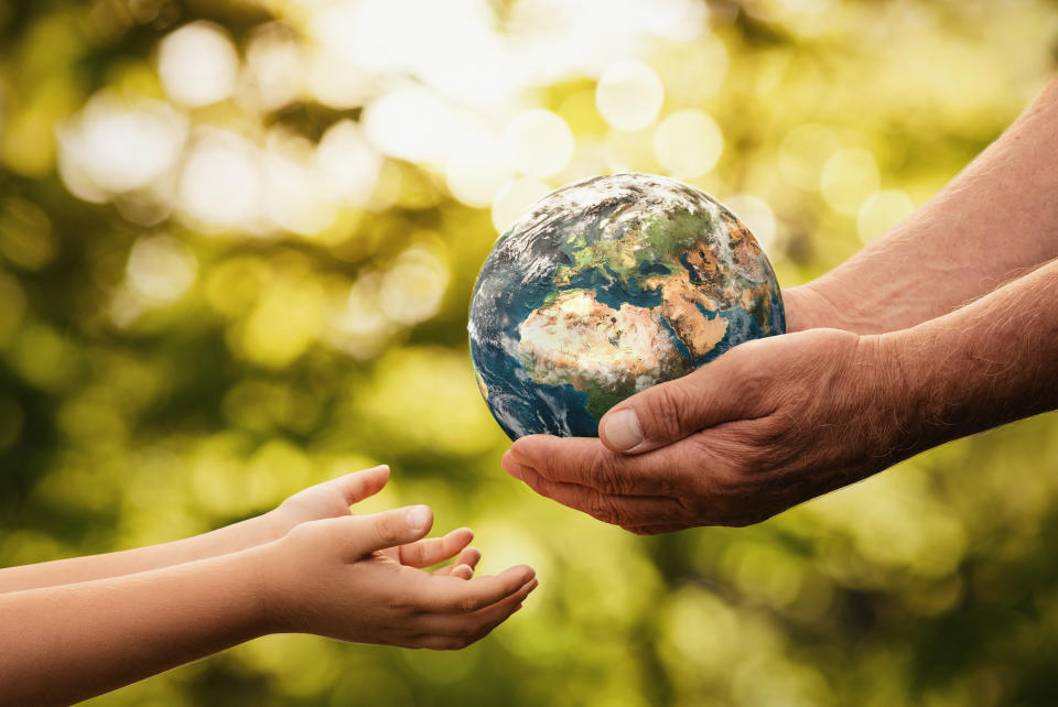 Close up of senior hands giving small planet earth to a child over defocused green background with copy space