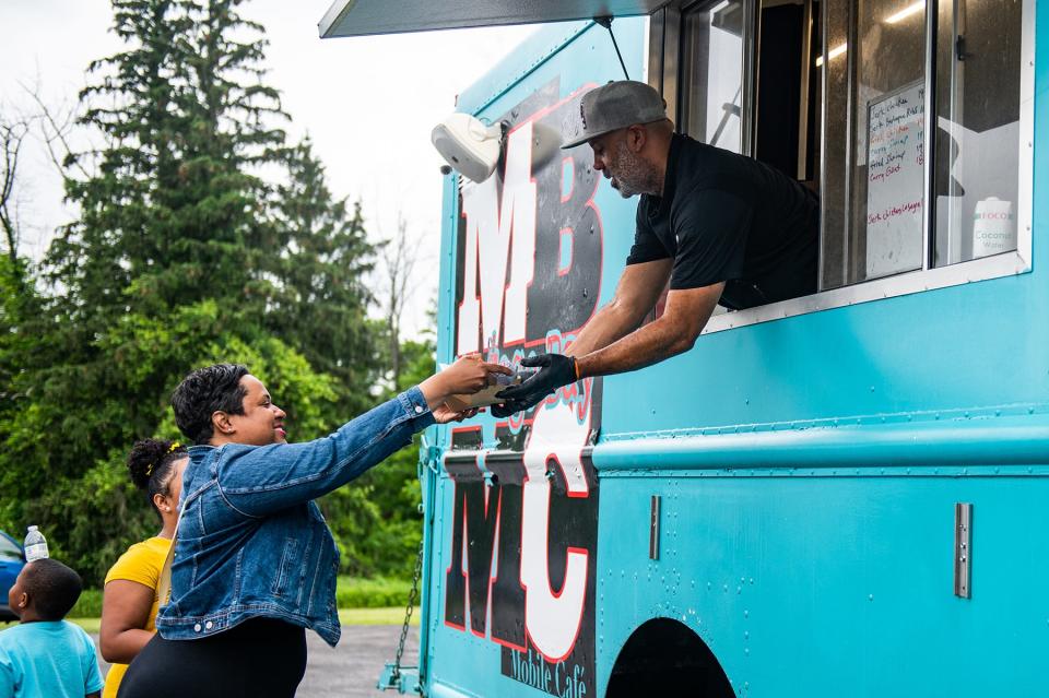 Robert Johnson, owner of Montego Bay Mobile Café, right, hands an order to Kim Benros of Monroe from his food truck in Harriman, NY on Thursday, June 16, 2022. Johnson cooks up Caribbean fusion food. KELLY MARSH/FOR THE TIMES HERALD-RECORD