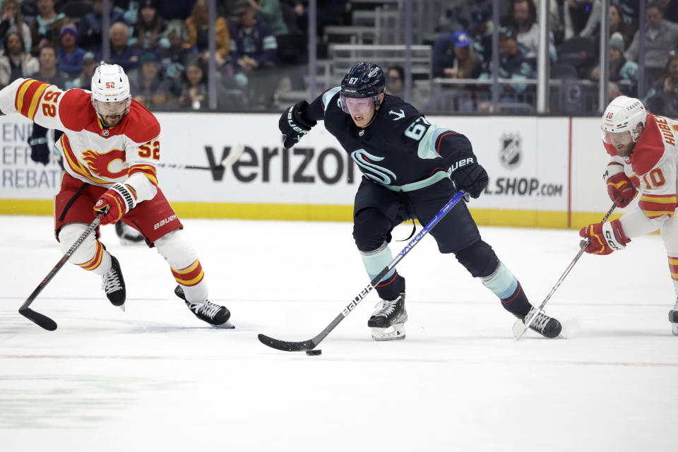 Seattle Kraken center Morgan Geekie (67) skates with the puck with Calgary Flames defenseman MacKenzie Weegar and center Jonathan Huberdeau (10) defending during the first period of an NHL hockey game Friday, Jan. 27, 2023, in Seattle. (AP Photo/John Froschauer)