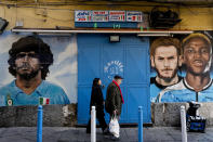 People walk past wall paintings of Napoli former and present soccer stars, from left, Diego Armando Maradona, Khvicha Kvaratskhelia and Victor Osimhen, in downtown Naples, Italy, Wednesday, April 19, 2023. It's a celebration more than 30 years in the making, and historically superstitious Napoli fans are already painting the city blue in anticipation of the team's first Italian league title since the days when Diego Maradona played for the club. (AP Photo/Andrew Medichini)