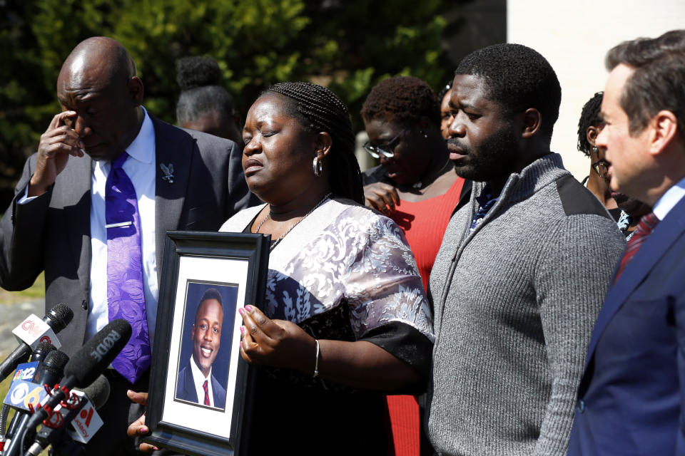 FILE - Caroline Ouko, mother of Irvo Otieno, holds a portrait of her son with attorney Ben Crump, left, her older son, Leon Ochieng and attorney Mark Krudys at the Dinwiddie Courthouse in Dinwiddie, Va., Thursday, March 16, 2023. Hours after a video was released publicly showing seven sheriff's deputies and three employees of a Virginia mental hospital pinning Otieno to the floor, attorneys for several of the defendants offered a possible glimpse at how they may defend them against second-degree murder charges. But Otieno's family and their lawyers, including prominent civil rights attorney Ben Crump, immediately pushed back against any attempt to minimize the role any of the defendants may have played in Otieno's death. (Daniel Sangjib Min/Richmond Times-Dispatch via AP , File)