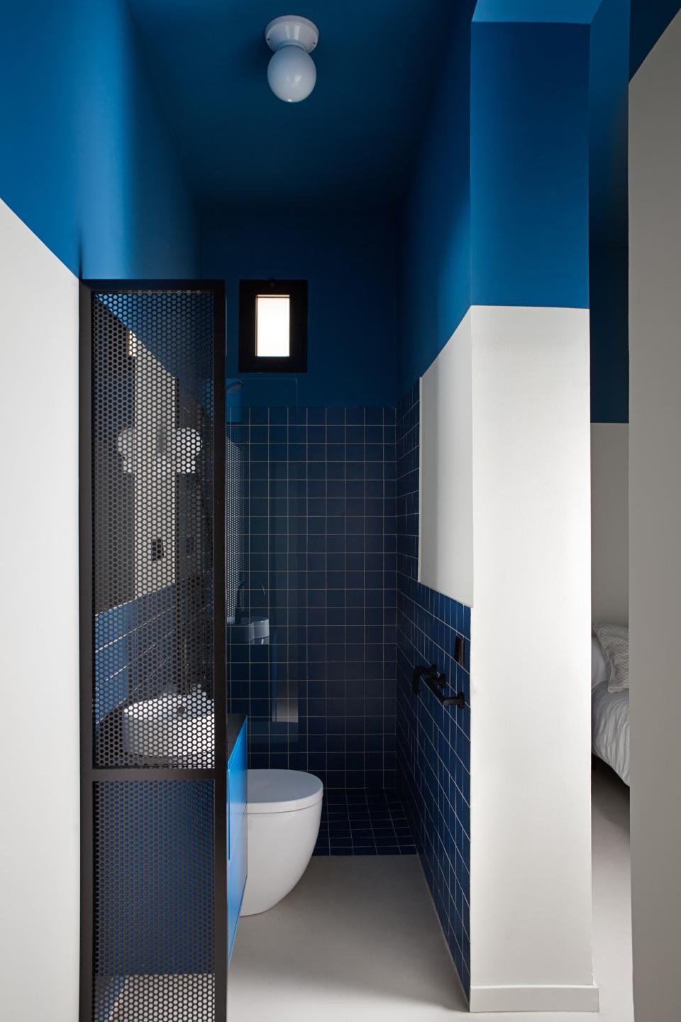 After: In the blue and beige room's adjoining bathroom, a bold painted ceiling makes the space appear much taller. Next to the sink, Ana and Enrique added a sliver of mesh to create some privacy without blocking the precious natural light coming from the bedroom window.