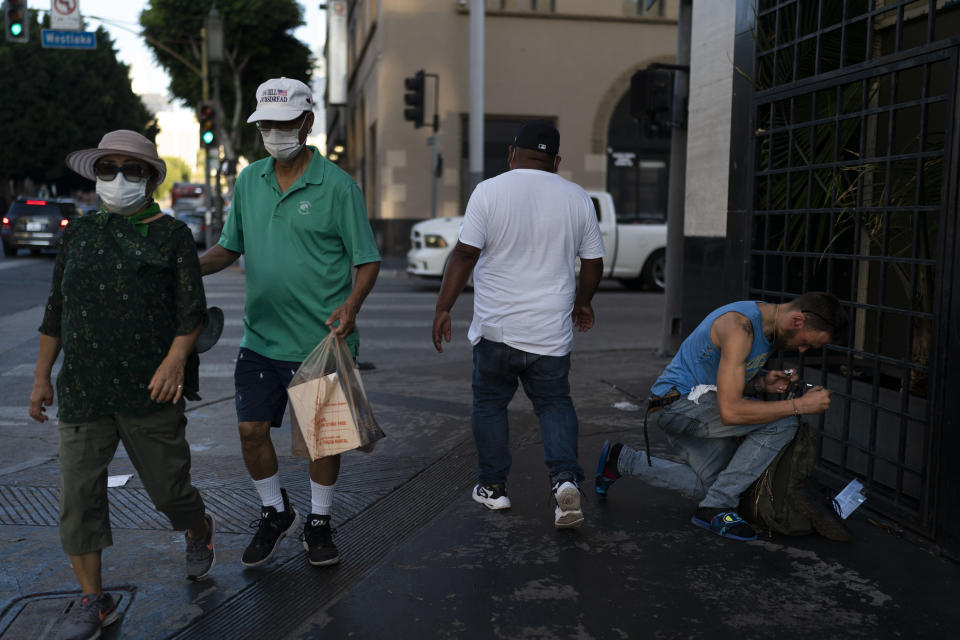 An addict kneels on a sidewalk to smoke fentanyl as pedestrians walk past him in Los Angeles, Thursday, Aug. 25, 2022. For too many people strung out on the drug, the sleep that follows a fentanyl hit is permanent. The highly addictive and potentially lethal drug has become a scourge across America and is taking a toll on the growing number of people living on the streets of Los Angeles. (AP Photo/Jae C. Hong)