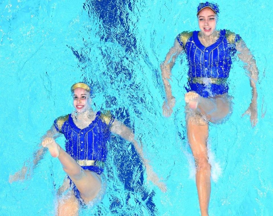 Two swimmers floating on their backs with one leg fully extended in the air