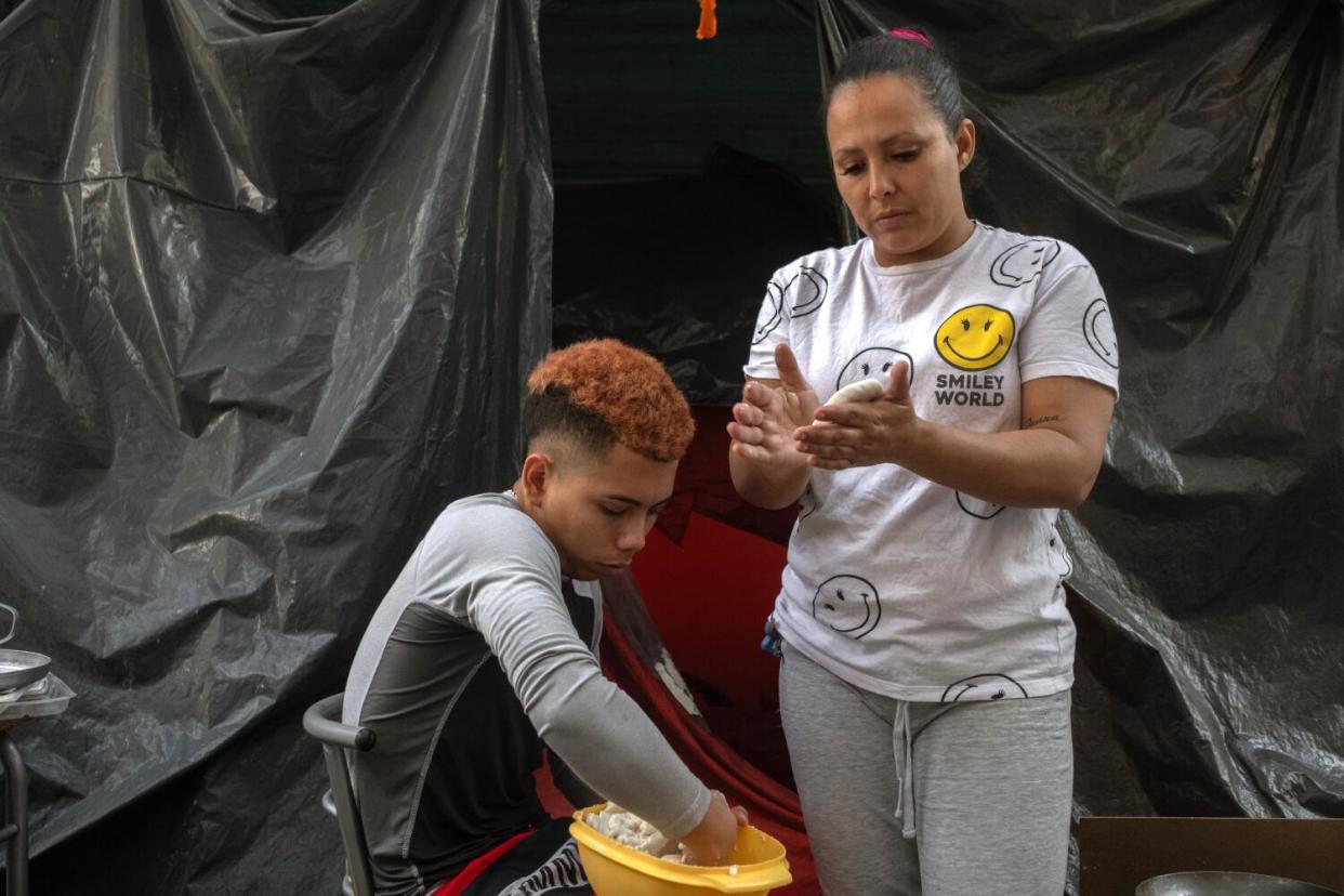 Karenis Alvarez, 36, and her 17-year-old son from Venezuela make arepas outside their tent in the Juarez