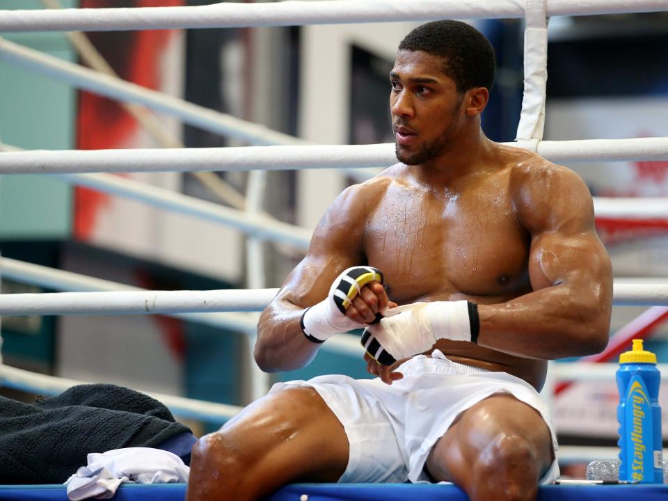 Anthony Joshua sitting on the edge of a boxing ring wrapping up his hands.