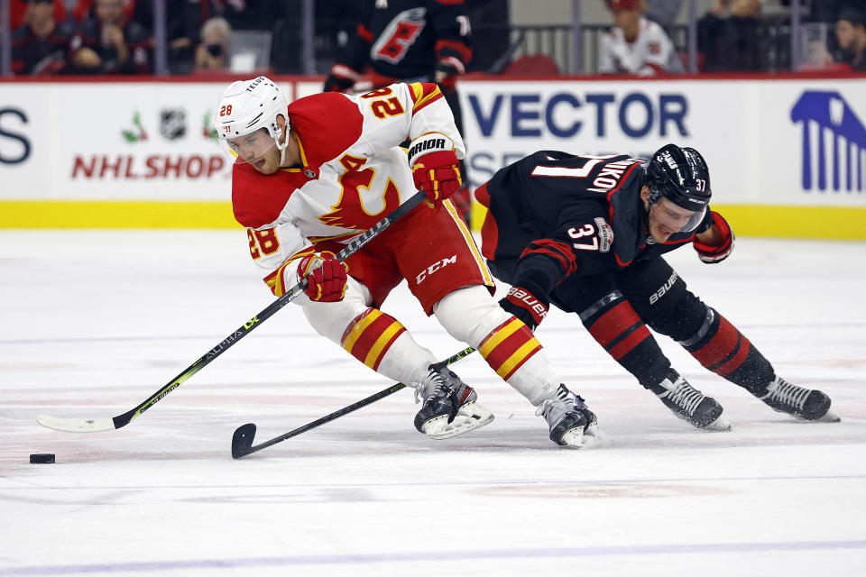 Calgary Flames' Elias Lindholm (28) skates the puck around Carolina Hurricanes' Andrei Svechnikov (37) during the second period of an NHL hockey game in Raleigh, N.C., Saturday, Nov. 26, 2022. (AP Photo/Karl B DeBlaker)