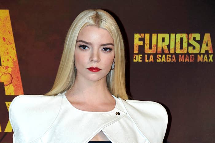 Anya Taylor Joy on red carpet in white outfit with structured shoulders, standing before a 'Furiosa' backdrop