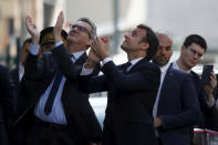 FILE - In this April 7, 2020 file photo, French President Emmanuel Macron, center, wearing no face mask, applauds residents with officials and body guard just beside him, after visiting a medical center in Pantin, near Paris. From the U.S. president to the British prime minister's top aide and far beyond, leading officials around the world are refusing to wear masks or breaking confinement rules meant to protect their populations from the coronavirus and slow the pandemic. While some are punished when they're caught, or publicly repent, others shrug off the violations as if the rules don't apply to them. (Gonzalo Fuentes/Pool via AP, File)