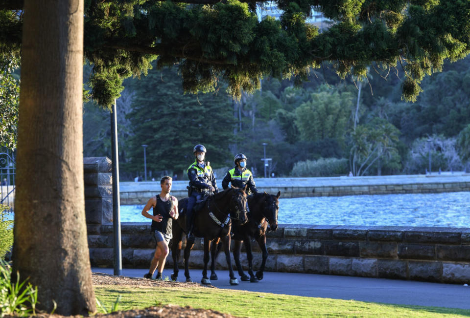 Two mounted police officers patrol around the edge of the harbour as a man runs past them doing his permitted exercise in Sydney, Australia. 