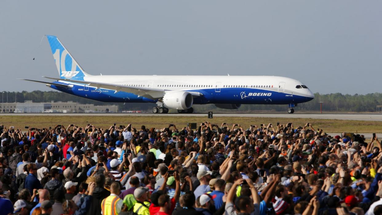 Boeing employees raise up their camera phones to record the first test flight of the new Boeing 787-10 Dreamliner