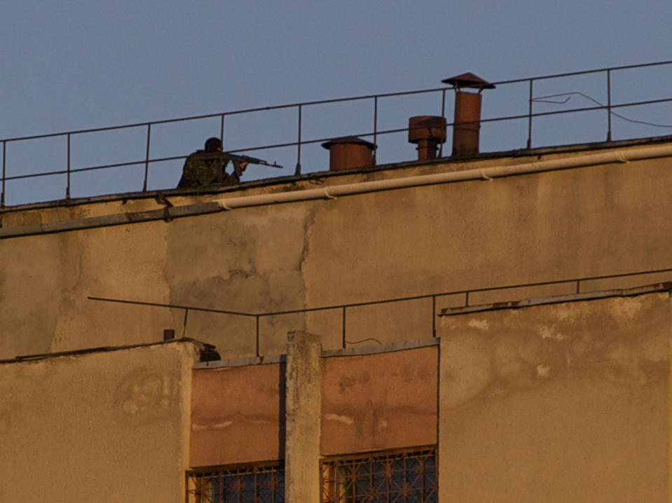 An armed man clears a roof of an Ukrainian military unit in Simferopol, Crimea, on Tuesday, March 18, 2014. A Ukrainian military spokesman says a serviceman has been killed and another injured when a base in Crimea was stormed by armed men. Vladislav Seleznev, a spokesman for the Ukrainian armed forces in Crimea, said on his Facebook page that the base in the Crimean capital Simferopol was stormed by unknown armed men on Tuesday. He said a truck bearing a Russian flag was used in the operation. (AP Photo/Ivan Sekretarev)