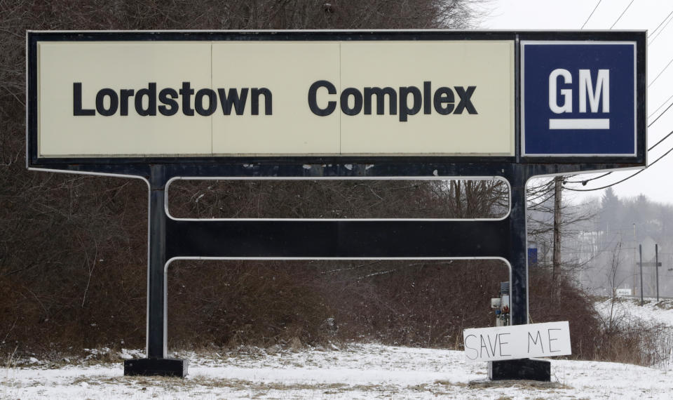 FILE - In this March 6, 2019 file photo, A "Save Me" sign rests against the Lordstown Complex sign in Lordstown, Ohio. The long-struggling Rust Belt community of Youngstown, Ohio, which was stung by the loss of the massive General Motors Lordstown plant this year, wants to become a research and production hub for electric vehicles.. But Youngstown faces competition from places like Detroit and China that are taking big roles in developing electric vehicles. (AP Photo/Tony Dejak, File)