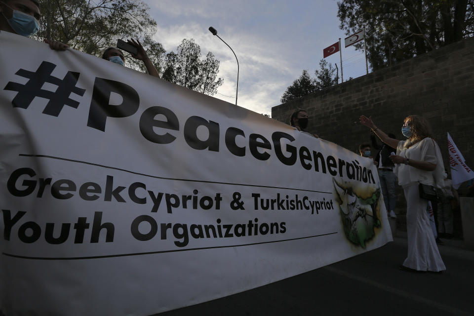 Greek Cypriots protestors hold a banner for peace as they march between the Turkish occupied area and the Geek Cypriots south, inside the U.N buffer zone during a peace protest in divided capital Nicosia, Cyprus, Saturday, April 24, 2021. United Nations Chief Antonio Guterres will host an informal gathering of the rival Greek Cypriot and Turkish Cypriot leaders as well as the foreign ministers of ethnically split Cyprus' ‘guarantors’ - Greece, Turkey and former colonial ruler Britain in Geneva - in hopes of getting the two sides to embark on a fresh round of formal reunification talks. (AP Photo/Petros Karadjias)