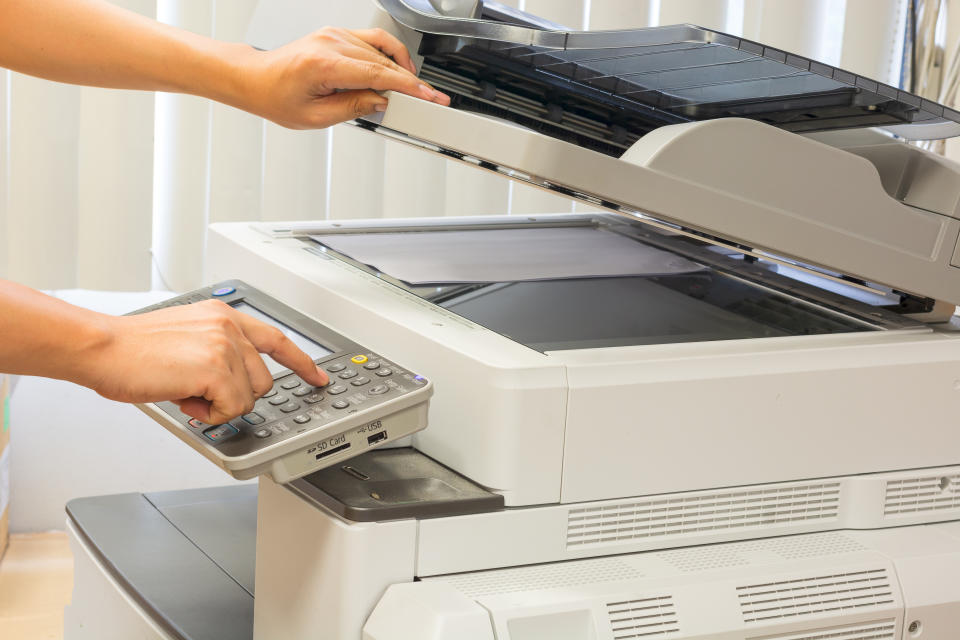 Person using a photocopy machine, placing a document on the scanner and pressing buttons on the control panel