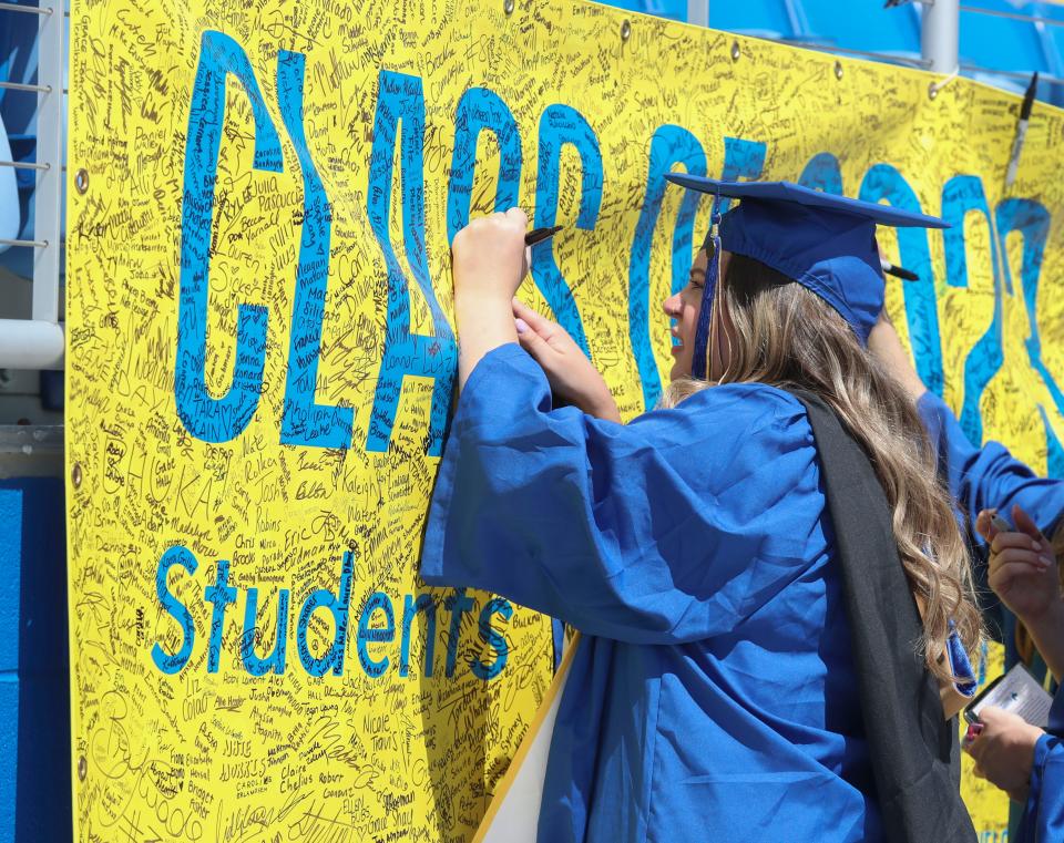 Marketing and advertising graduate Nicole Richter of Dumont, New Jersey, makes her mark as members of the Class of 2023 sign a banner following the University of Delaware's 2023 Commencement at Delaware Stadium, Saturday, May 27, 2023.