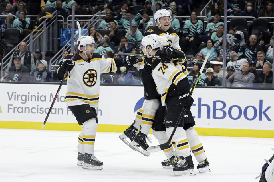 Boston Bruins defenseman Matt Grzelcyk, left, Charlie McAvoy, top, and a teammate celebrate a goal by left wing Jake DeBrusk (74) against the Seattle Kraken during the third period of an NHL hockey game Thursday, Feb. 23, 2023, in Seattle. The Bruins won 6-5. (AP Photo/John Froschauer)