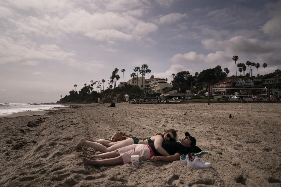 Drue Burkey and his girlfriend Reace Hammel sunbathe in Laguna Beach, Calif., Monday, May 17, 2021. California won't lift its mask requirement until June 15 to give the public and businesses time to prepare and ensure cases stay low, state Health Director Mark Ghaly said Monday. (AP Photo/Jae C. Hong)