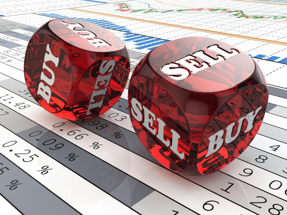 Two red dice reading Buy and Sell rolling across paperwork displaying financial data and stock charts.