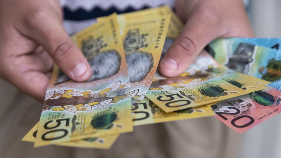 Male person holding some Australian currency. This visual concept evokes ideas around saving money, paying for expenses and investments.