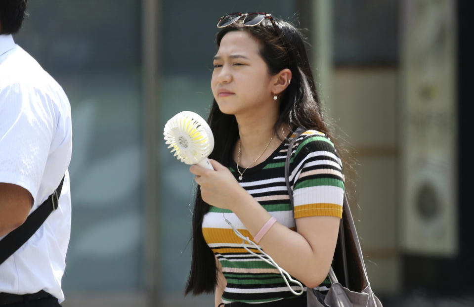 FILE - A woman holds a portable fan in Tokyo, Monday, July 23, 2018, as searing hot temperatures are forecast for wide swaths of Japan and South Korea in a long-running heat wave. (AP Photo/Koji Sasahara, File)