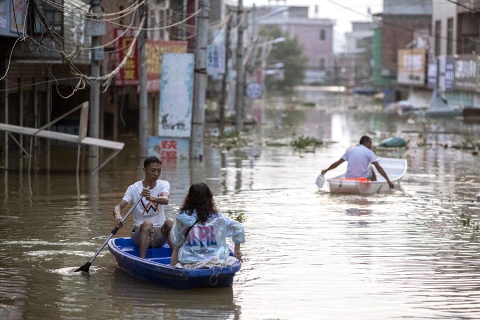 Villagers paddle boats through the flooded main street of Dixi village at dusk.