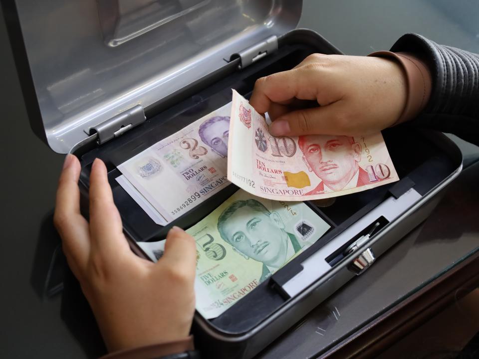 hands of a woman holding singaporean money to keep it in a box