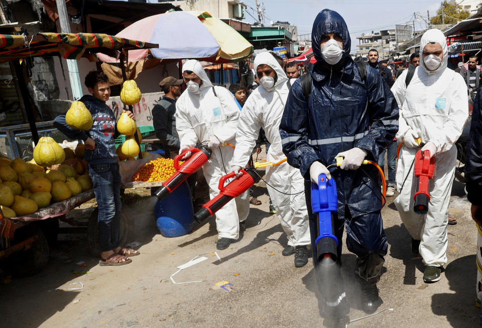 FILE - In this Thursday, March 19, 2020 file photo, workers wearing protective gear spray disinfectant as a precaution against the coronavirus, at the main market in Gaza City. The Gaza Strip has been largely cut off from the rest of the world for more than a decade by an Israeli-Egyptian blockade. But the coronavirus has found a way in. Fearing a widespread outbreak after nine confirmed cases, Gaza’s Hamas leaders are racing to build two massive quarantine complexes and prepare the overcrowded territory not equipped to deal with a new health crisis. (AP Photo/Adel Hana, File)