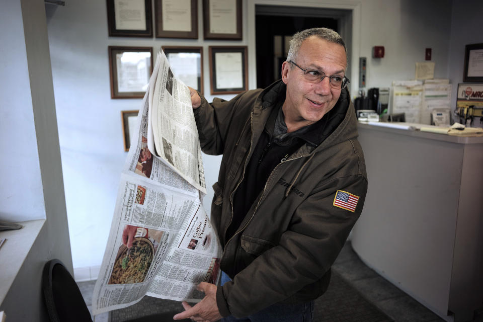 In this Wednesday, April 10, 2019 photo Phil Viscuso, owner of East Street Auto Sales, flips through a copy The Berkshire Eagle Newspaper at his shop in Pittsfield, Mass. Viscuso said he has two subscriptions of the print edition of The Berkshire Eagle newspaper so his customers can read the paper while waiting for their cars. (AP Photo/Steven Senne)
